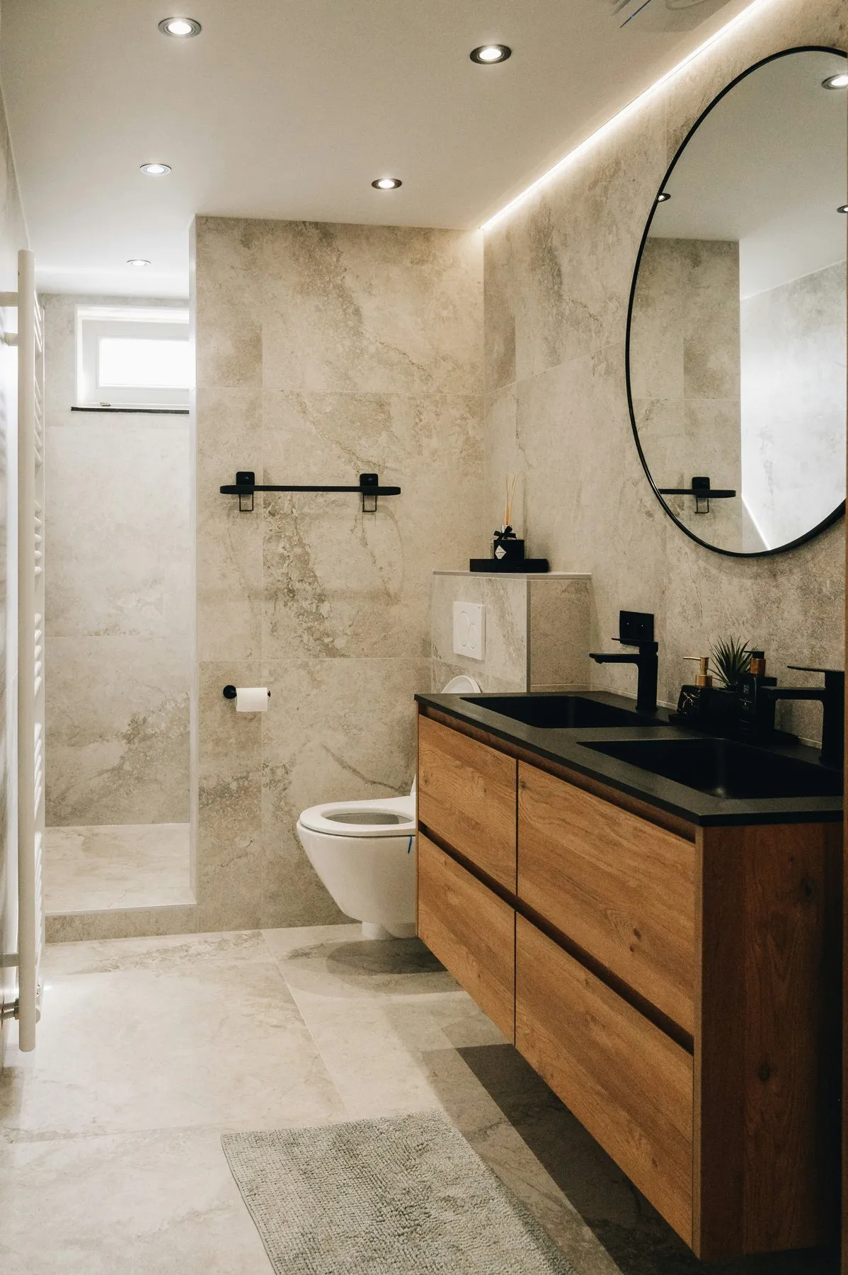 Travertine bathroom with black fixtures and a round mirror
